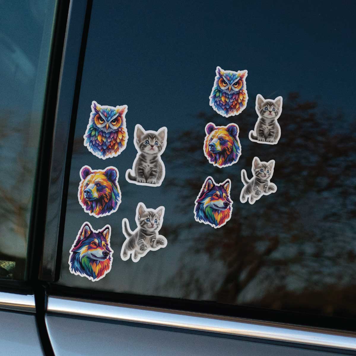 Farebné nálepky s motívmi sovy, medveďa, vlka a mačiatok sú nalepené v dvoch radoch na tmavom bočnom okne sivého vozidla.